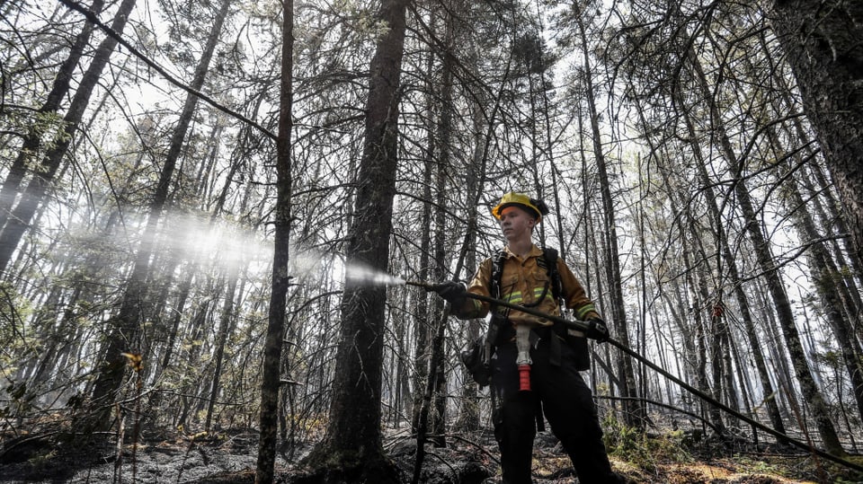 Feuerwehrmann sprüht Wasser in verbrannter Umgebung