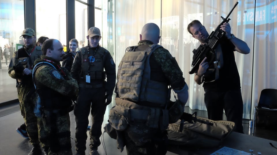 Männer in Uniformen, einer kontrolliert ein Gewehr.