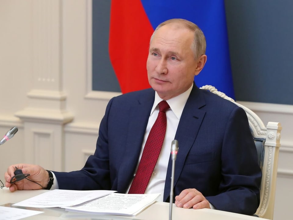 Putin sitzt an einem Tisch. Vor ihm liegt ein Dokument und es hat zwei Mikrofone.