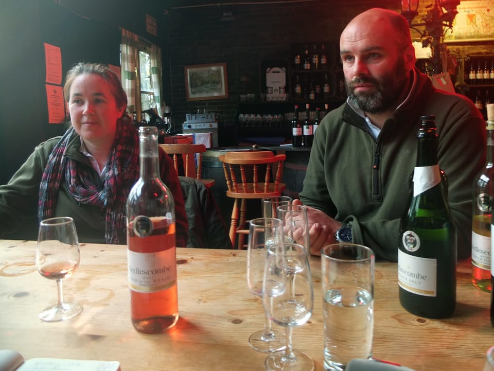 Eine Frau und ein Mann sitzen an einem Tisch, auf dem eine Weinflasche steht.