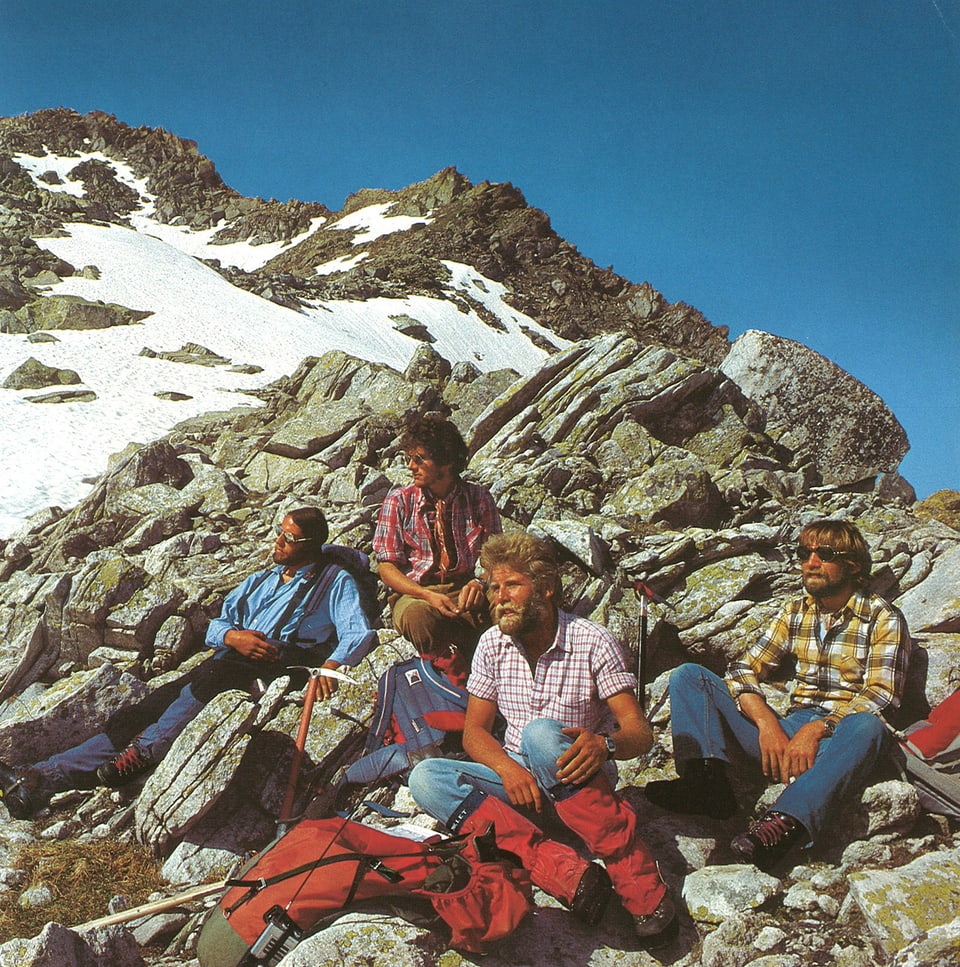Die vier Alpinisten sitzen in den Bergen auf ein paar Felsen und ruhen sich aus.