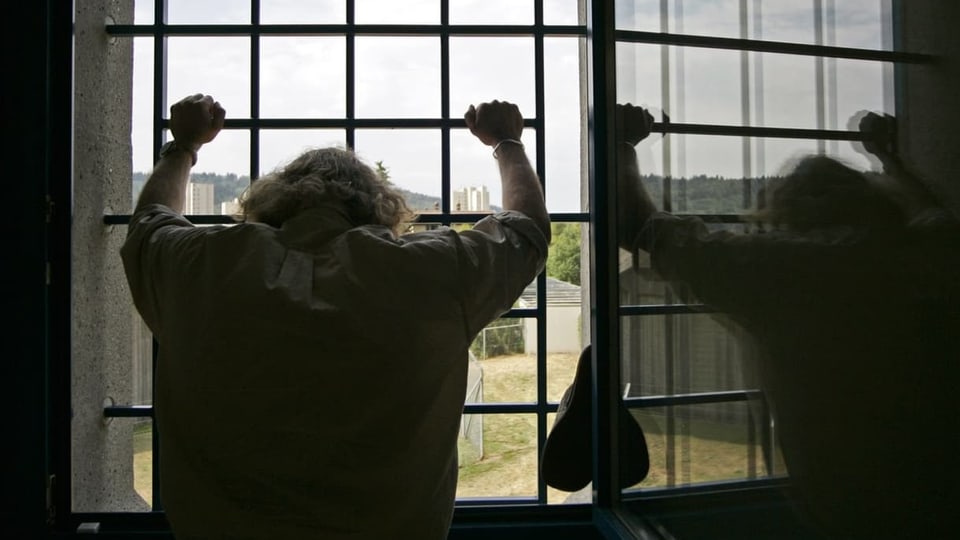 Ein Mann steht vor einem Gitter und schaut aus dem Gebäude. 