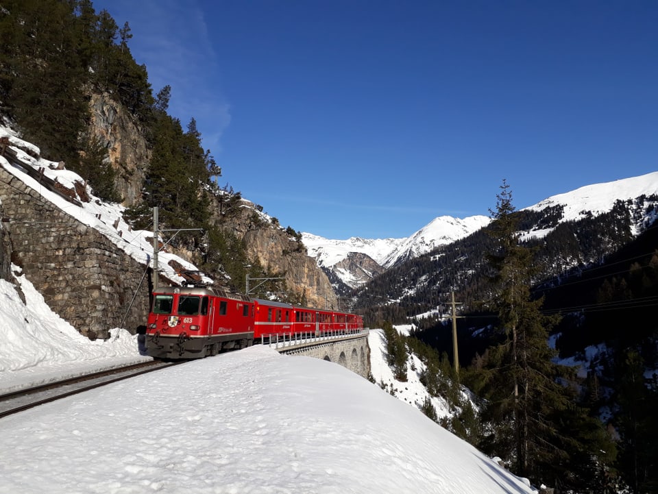 Ein roter Zug der Rhätischen Bahn fährt durch eine verschneite Landschaft.