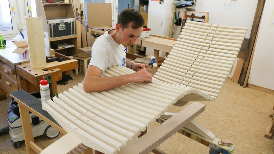 ein junger Mann baut ein Liegestuhlgerüst aus Holz