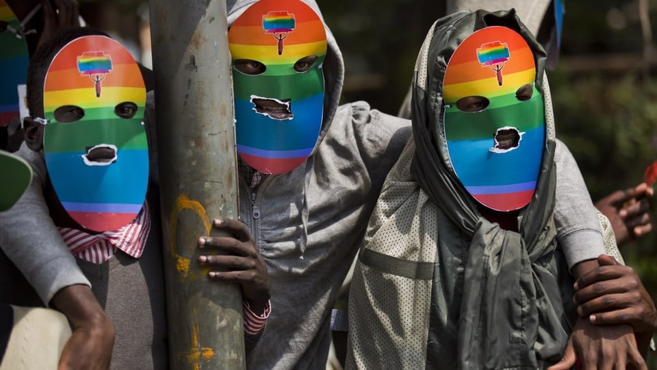 Drei Personen mit regenbogenfarbigen Masken an einer Demonstration