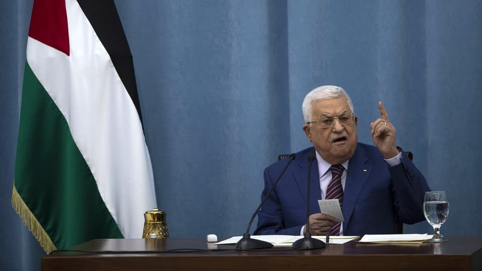 Mahmoud Abbas sitzt am Tisch und hält eine Rede mit gehobenem Finger. Dahinter eine Palästina-Fahne.