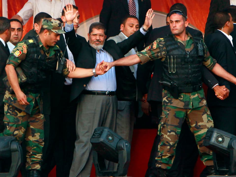 Mursi hebt nach seinem Sieg als neuer Präsident Ägyptens die Hände in die Hühe, Soldaten beschützen ihn.  