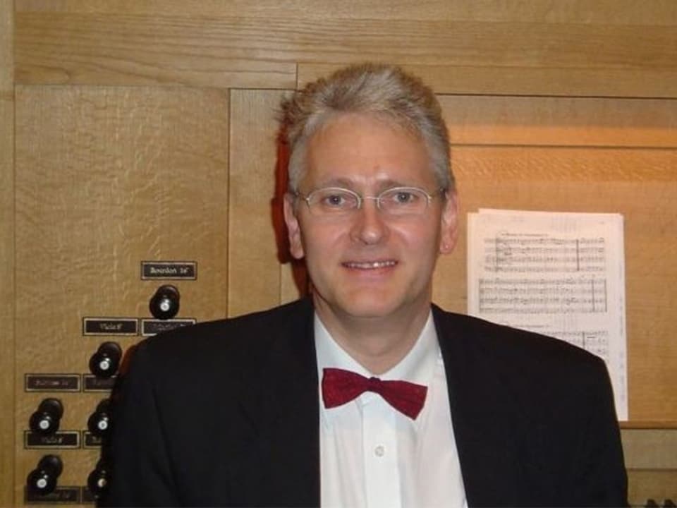 Markus Kühnis im Anzug mit roter Fliege vor einer Orgel.