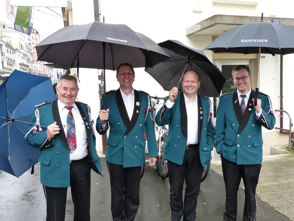 Uniformierte Blasmusikanten unter Regenschirmen.