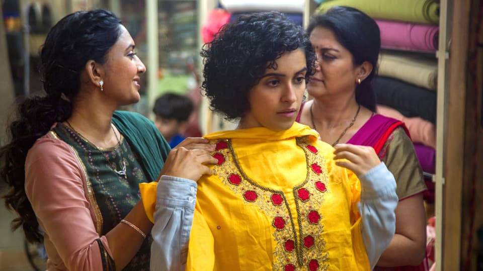 Eine indische Frau im Kleiderladen: sie hält ein Kleid vor sich hin und steht vor einem Spiegel.