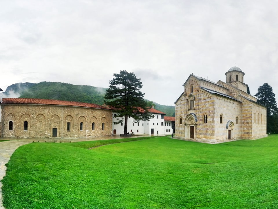 Klostergebäude mit Kirche umgeben von Wiesen und Bäumen.