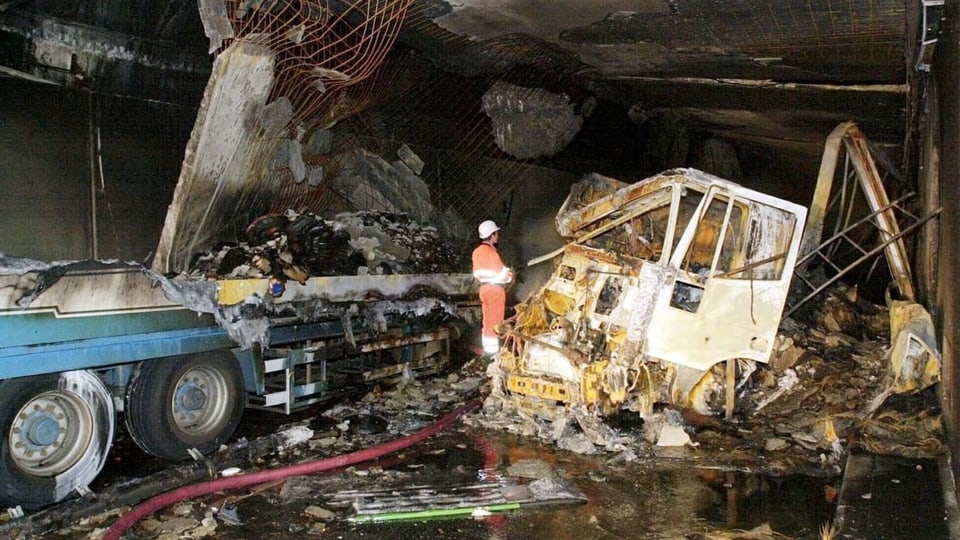 Zwei Wracks von Lastwagen sind voll mit Asche und komplett zerstört in einem dunklen Tunnel.