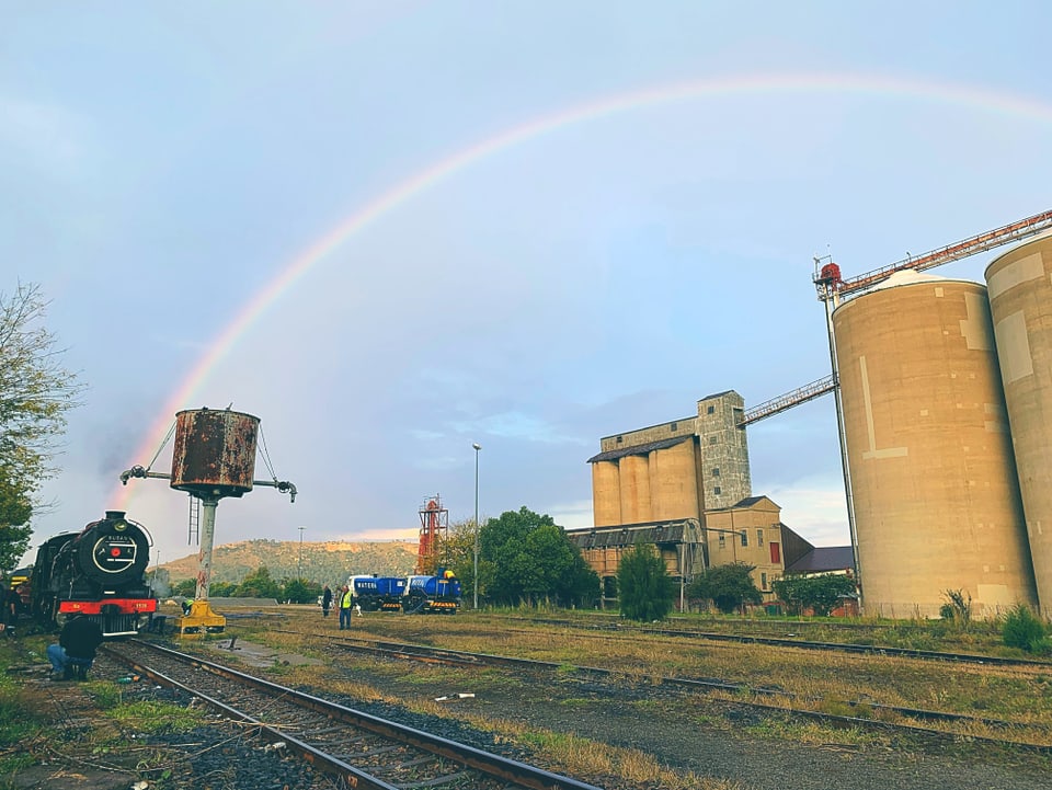 Lokomotive und alte Fabrikgebäude in Südafrika unter einem Regenbogen.