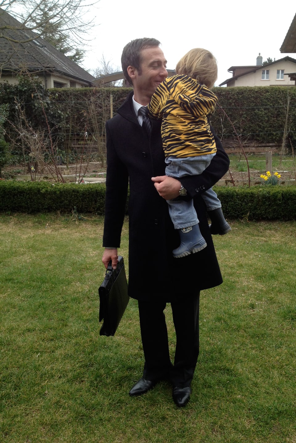 Elias Bartlome haät seinen Sohn Anatol auf seinem Arm. Sie stehen im Garten.