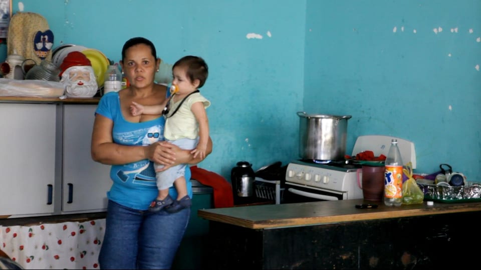 Eine Frau steht mit einem Baby auf dem Arm in einer behilfsmässigen Küche.