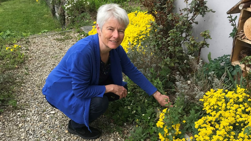 Sandra Lutz kniet vor einem gelben Strauch in ihrem Garten.