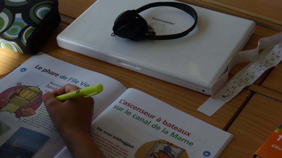 Ein Schüler schreibt in ein Heft. Vor ihm liegt ein Laptop.