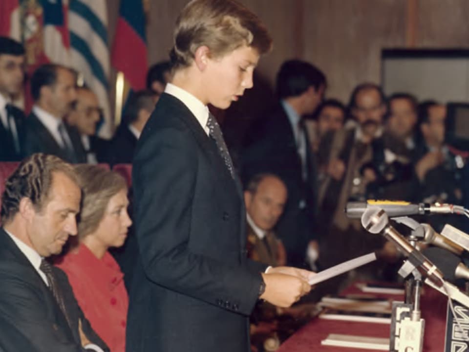 Prinz Felipe als Knabe am Mirkofon stehen. Im Hintergrund sitzen König Juan Carlos und Königin Sophia.