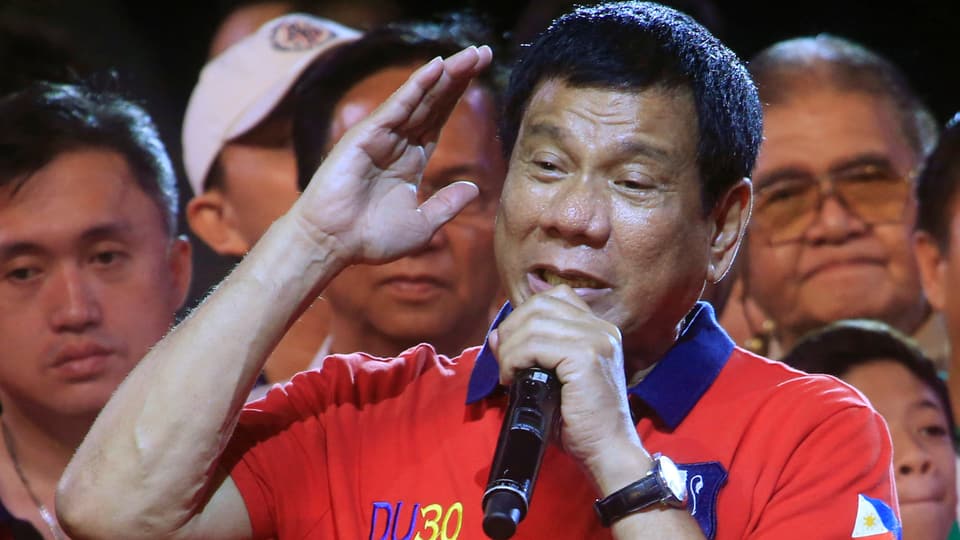 Rodrigo Duterte in einem roten Polo-Shirt und mit einem Mikrofon in der linken Hand.