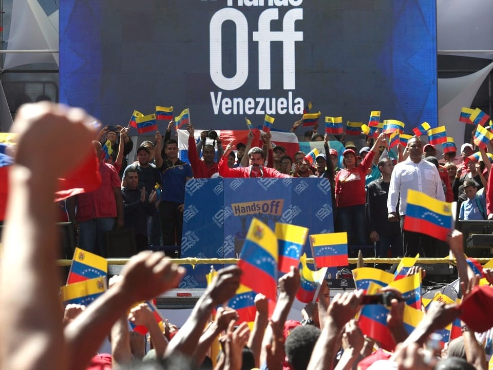 Maduro an Rednerpult. Vor ihm heben Hunderte die Faust. Überall Fahnen.