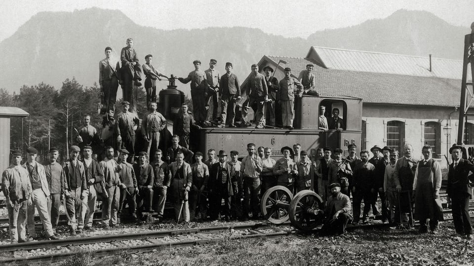 Altes schwarz-weiss Bild von einer grossen Gruppe Eisenbahnarbeitern die auf einer Lock fürs Foto posieren