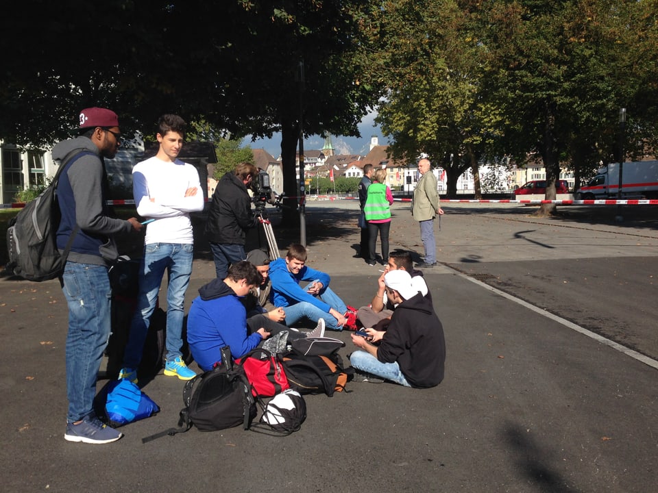 Evakuierte Schüler sitzen vor dem abgesperrten Gelände. 