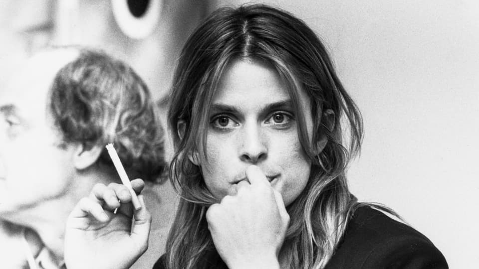 Eine junge Frau hält in der einen Hand eine Zigarette, die andere Hand hält sie am Mund.