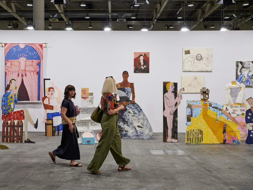 Zwei Besucherinnen laufen an bunten Kunstwerken der Art Basel vorbei,