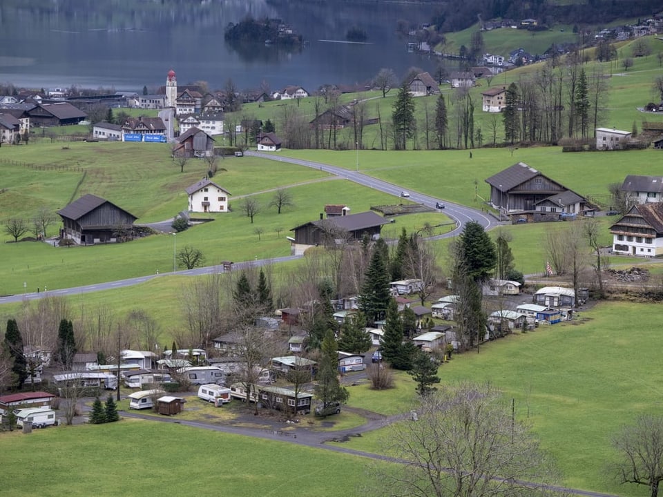 Luftaufnahme eines Dorfes mit Campingplatz, Kirche und Seeufer im Hintergrund.