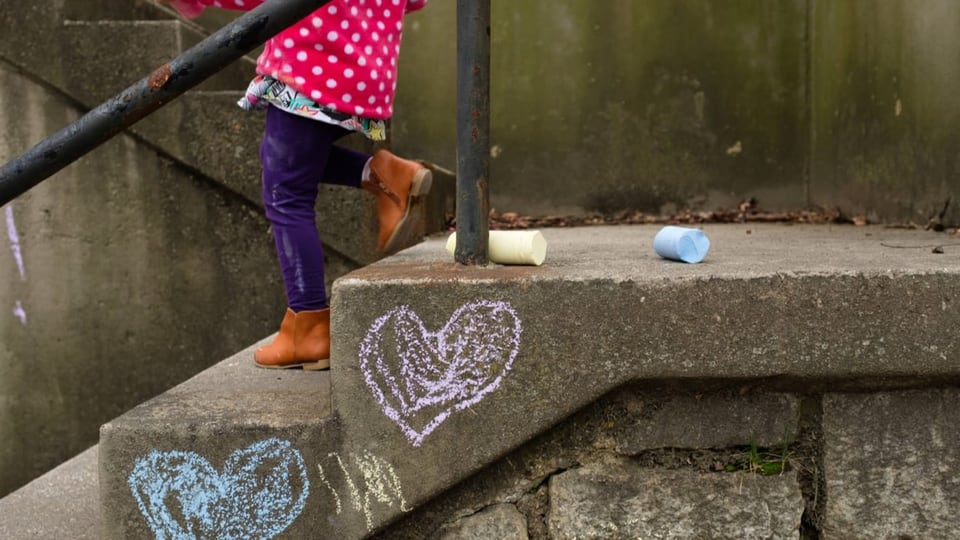 Kind geht draussen eine Treppe herunter, auf der mit Kreide Herzen gezeichnet sind.