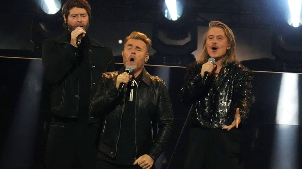 Drei Männer der Band Take That  singen auf einer Bühne.