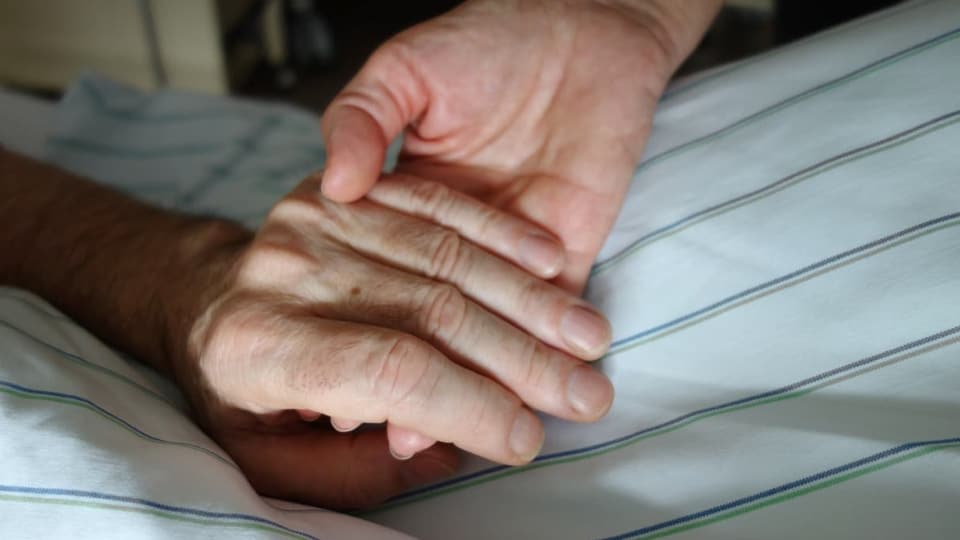 Pflegeperson hält die Hand einer Patientin, eines Patienten