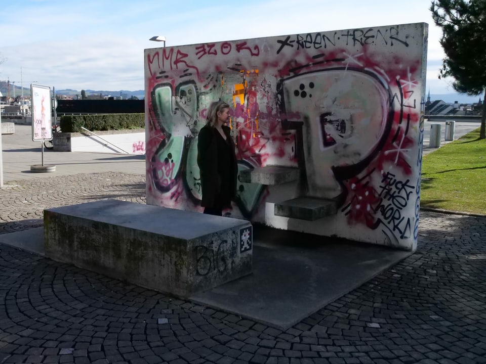 Frau steht vor einem Kunstwerk - einer Betonmauer mit Graffitis
