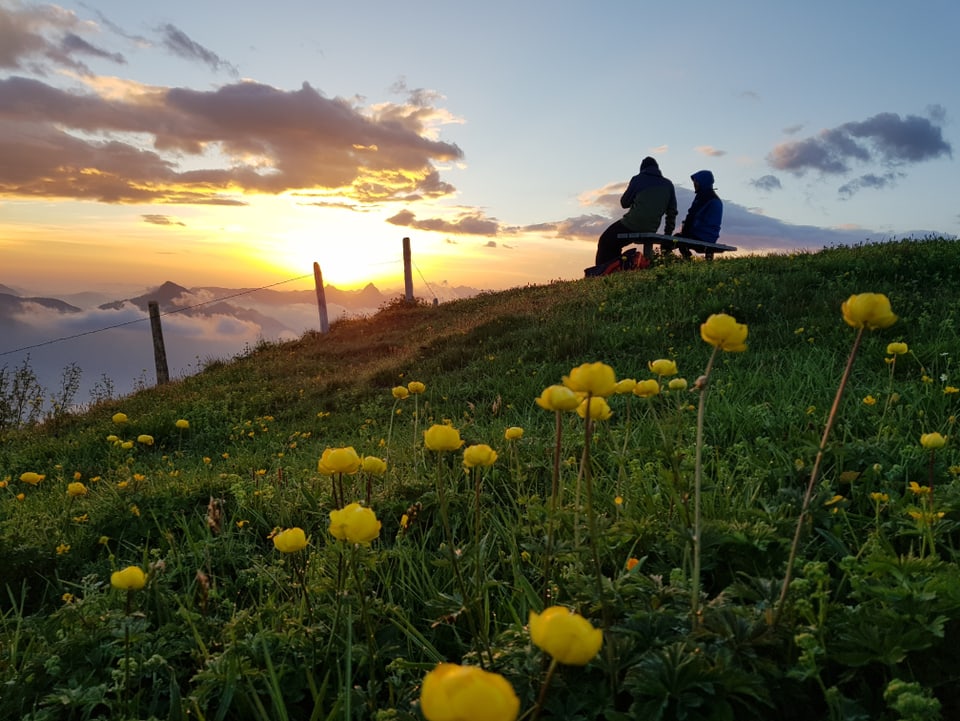 Zwei Menschen auf einer Bank bestaunen den Sonnenaufgang über den Bergen.