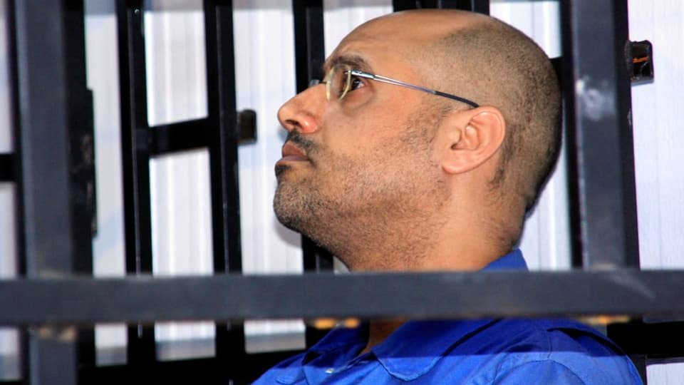 Saif al-Islam Gaddafi sitzt hinter Gitter und hört konzentriert zu.
