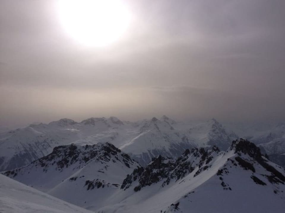 Verschneite Alpen mit diffusem Licht wegen dem Staub in der Luft. Sonne ist als Scheibe zu erkennen. 