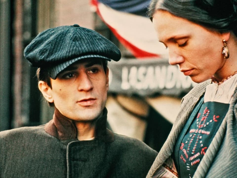 Robert De Niro in jungen Jahren mit einem blauen Hut schaut eine Frau an, welche man rechts vorne im Vordergrund sieht.