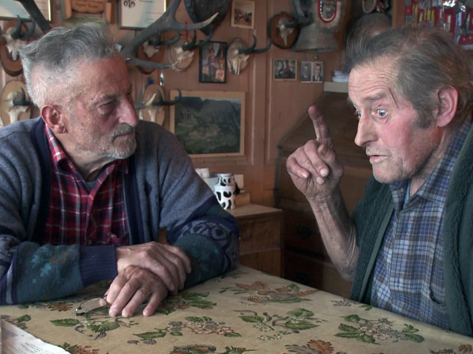 Die beiden Bauern Remigi Bissig und Sepp Stadler unterhalten sich am Tisch sitzend.
