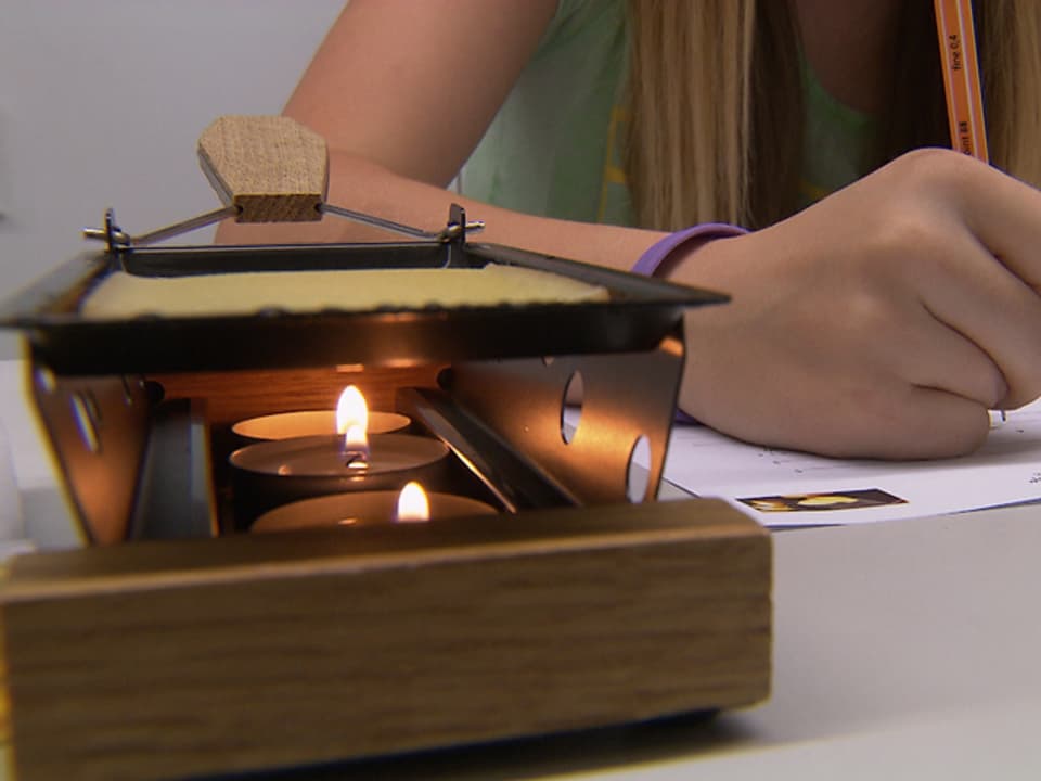 Neben einem brennenden Raclette-Öfeli macht sich eine Schülerin Notizen.