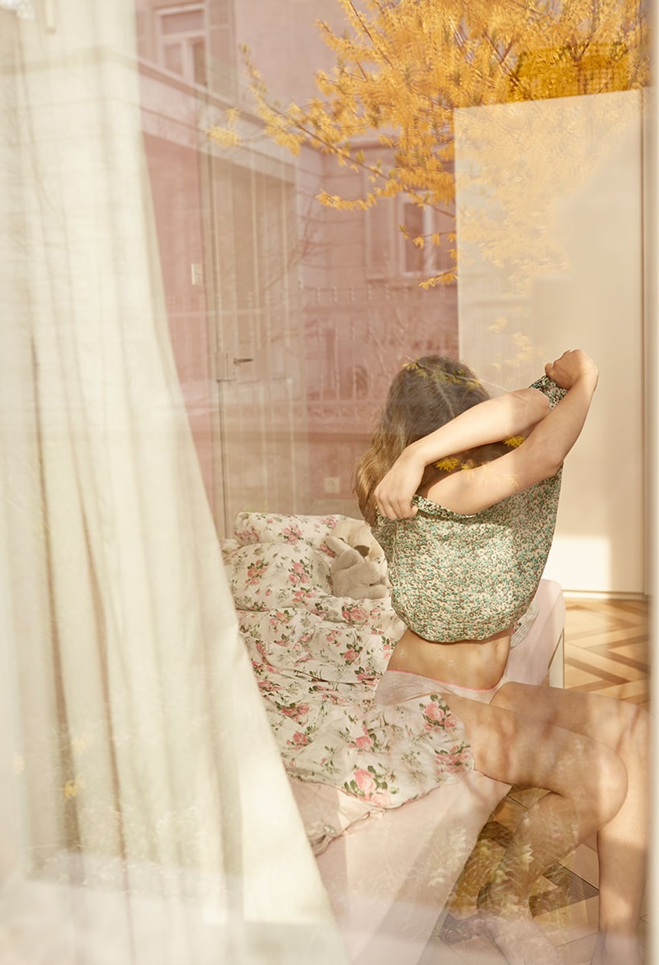 Durch ein Fenster sieht man ein Mädchen, dass sich den Pullover auszieht.