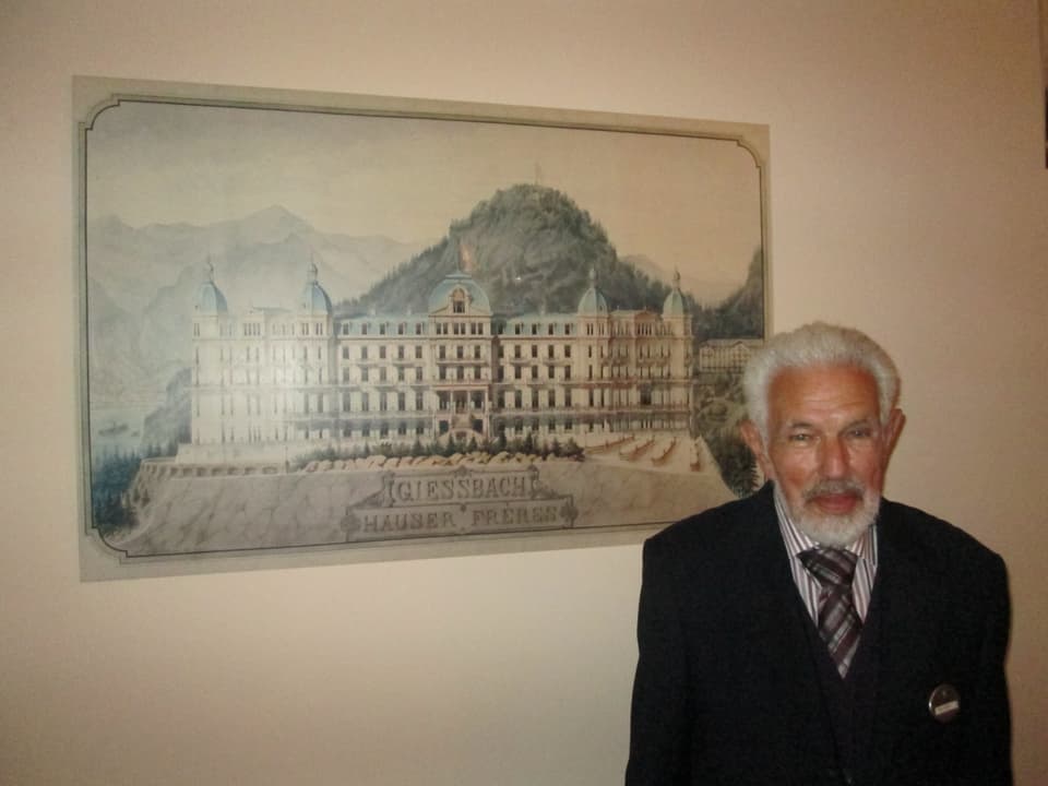 Ein Mann mit weissem Haar und Bart steht auf einem Bild des Grand Hotels.