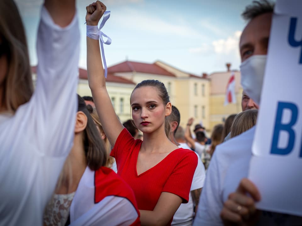 Eine junge Frau in rotem Kleid bei einer Demo. Sie hält die Faust hoch.