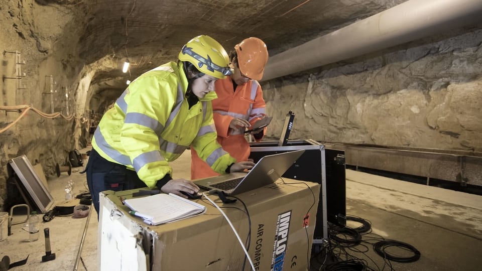 Zwei Forscher im Tunnel schauen auf einen Laptop.