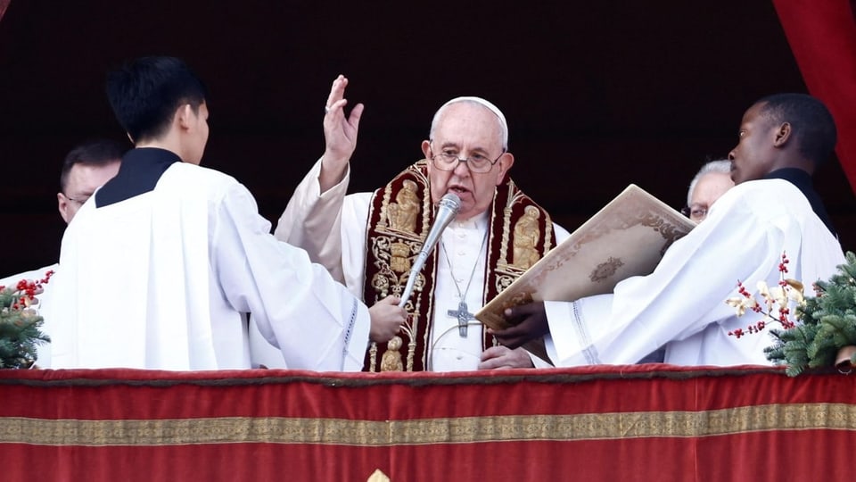 Papst spricht vor Menge, zwei Männer halten Tafeln vor ihm
