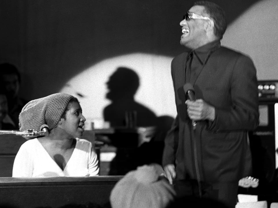 Aretha Franklin am Klavier, daneben steht Ray Charles mit Mikrofon.