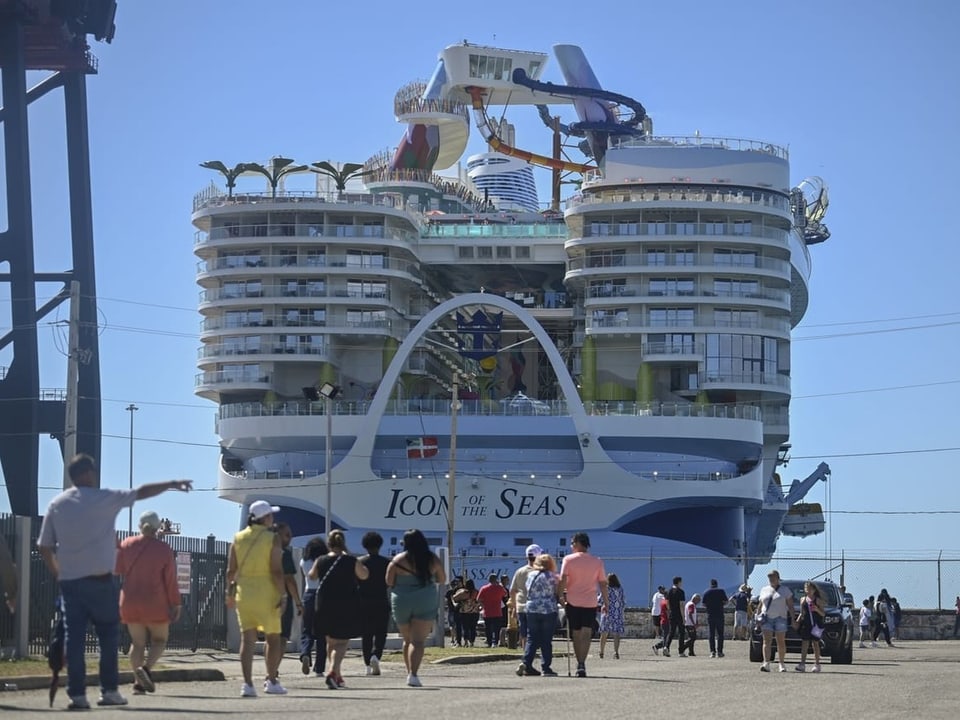 Menschen laufen am Hafen und bestaunen das riesige Schiff.