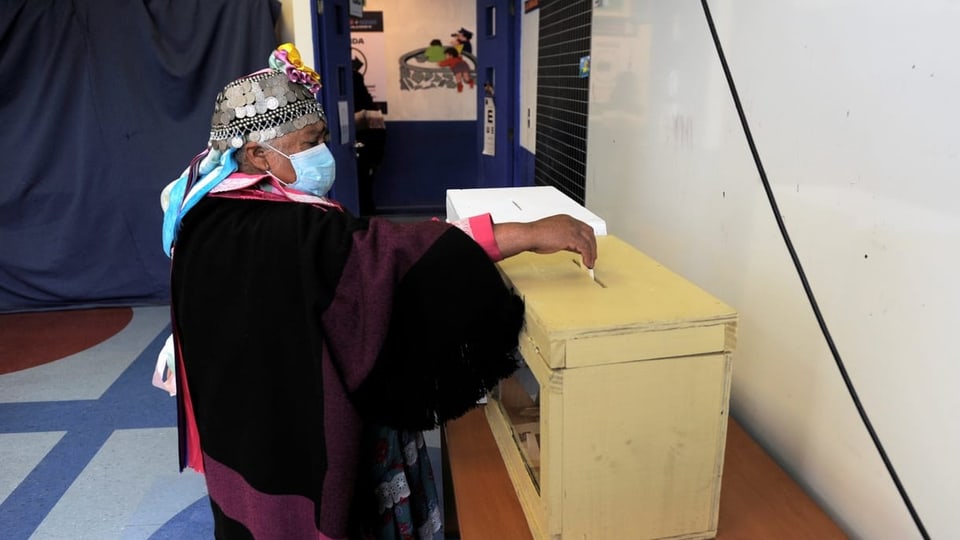 Frau legt Wahlzettel in Urne.