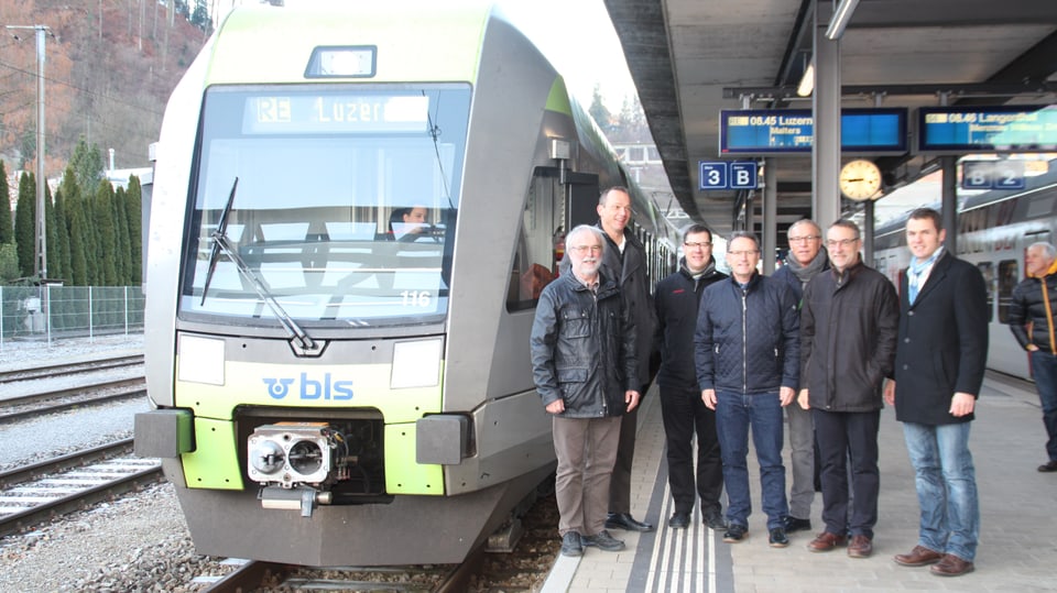 Gruppe von Männern steht an einem Bahnhof neben einem modernen Zug.