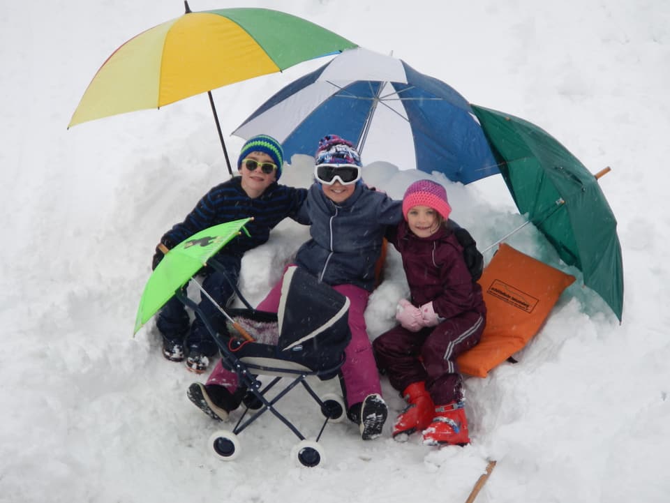 Drei Kinder mit Sonnenschirmen im Schnee.