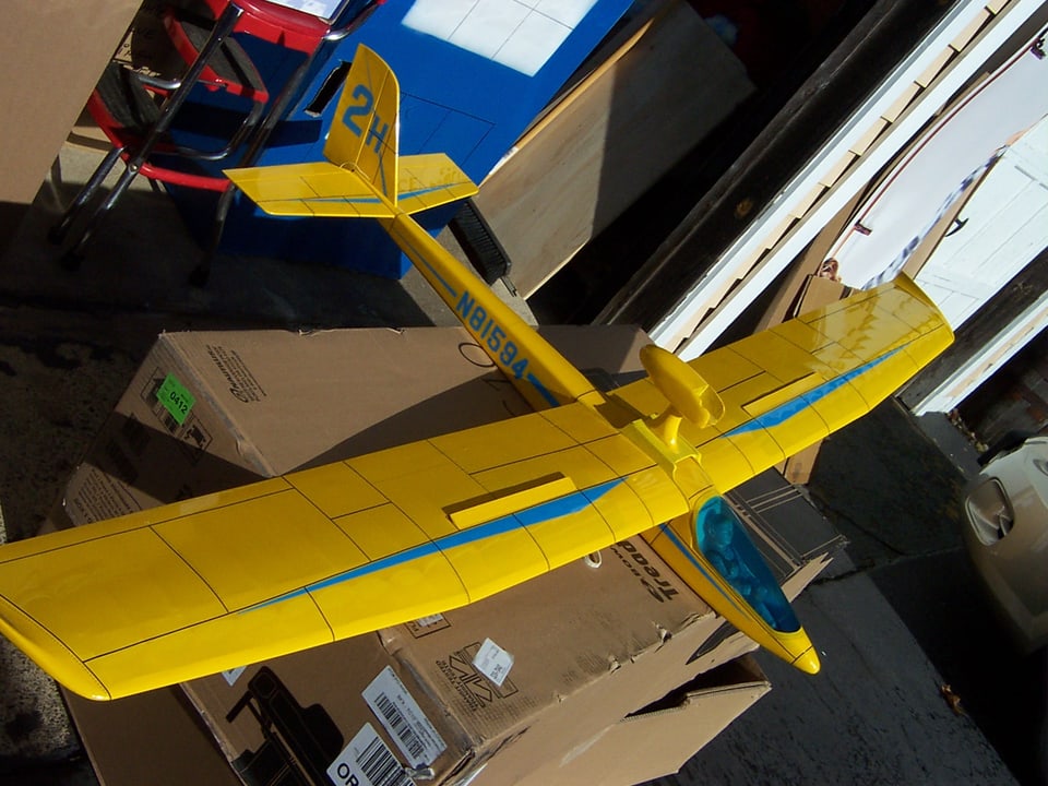 Ein gelbes Segelflugzeug liegt auf einer Kartonkiste.